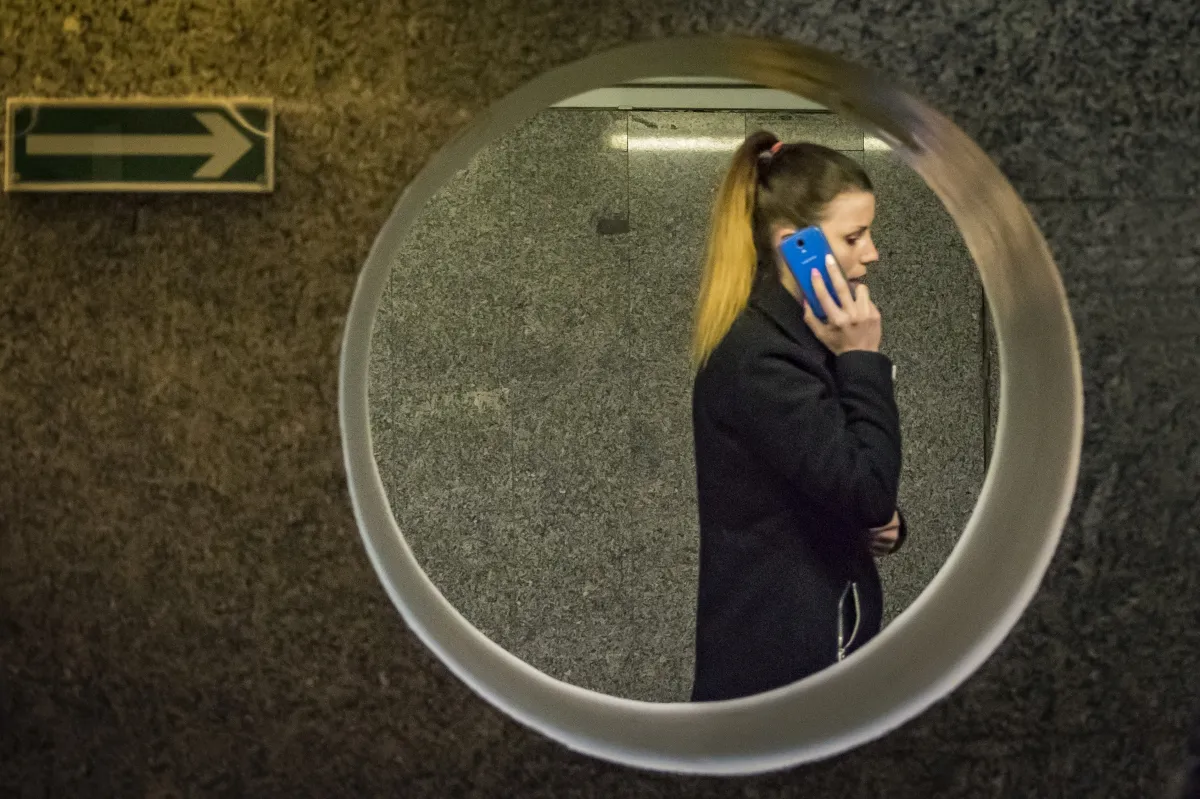 Woman talking on a blue phone reflected in a circular wall mirror